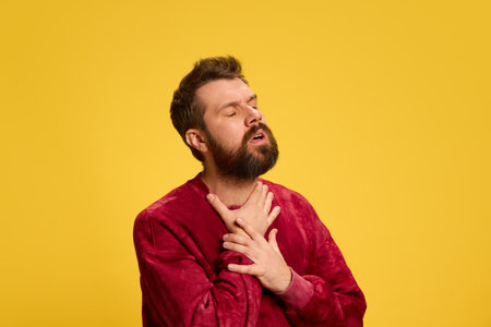 Young man feels badly, first symptom of sickness sore throat against yellow studio background. Epidemic. Concept of healthcare, medicine, infection and treatment. Ad.の写真素材