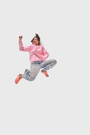 Woman in casual pink and denim leaps mid-air with joyful expression, showcasing energy and motion...