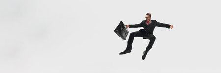 Banner. Businessman in black suit and red tie mid-air, holding black briefcase flying against white studio background with copy space. Concept of success, professional development, movement. Adの写真素材