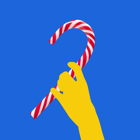 Contemporary art collage. Yellow hand holds candy cane against a bright blue background. Minimalist composition, bold colors. Festive and playful image. Concept of winter season, holidays.の写真素材