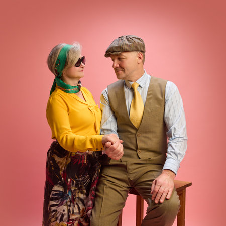 Man and woman hold hands with warm smiles, man in vest and yellow tie, woman in yellow blouse and scarf, both looking at each other. Concept of mature people in modern lifestyle, fashion. Adの写真素材