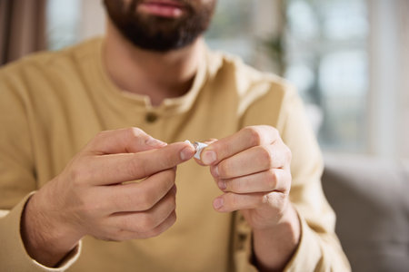 Close up view of man, squeezing cream out of small tube with hand sitting on sofa in living room. Colds and home treatments. Concept of illness, pharmaceutical, medicine.の写真素材