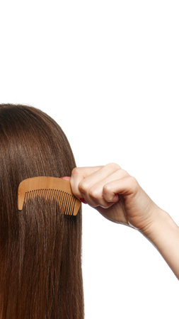 Close-up of hand combing long, smooth hair with wooden comb against white background, representing...