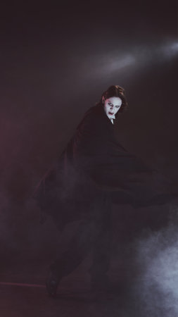 Man with pale face and cape, looks as vampire, spins dramatically, shows terrifying sharp fangs, in...