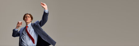 Banner. Successful happy young man dancing, raising hands with joy against grey studio background with negative space to insert text. Concept of human emotions, self-expression. Adの写真素材