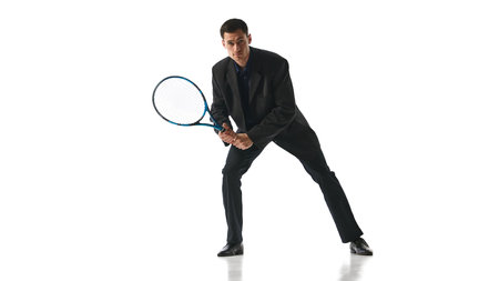 Man in black suit holding tennis racket in defensive stance, reflecting readiness to handle unexpected challenges in corporate world. Concept of business, work-life balance, leadership, multitasking.の写真素材