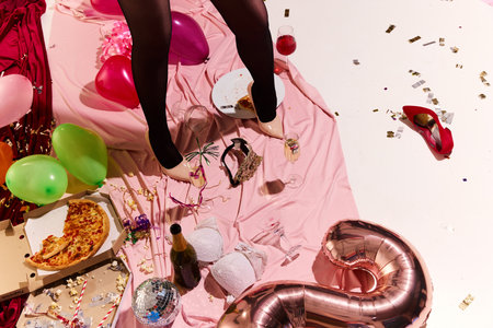 Messy afterparty floor with pink satin, green balloons, crushed confetti, spilled drinks, and woman in high heels showcases wild night turned into morning regret. Concept of alcohol, hangover.の写真素材