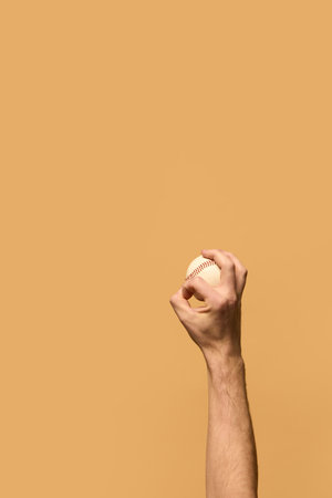 Hand gripping baseball tightly, fingers positioned for pitch, showcasing technique and focus in sports against warm-toned background. Concept of sport equipment, control, strategy.の写真素材