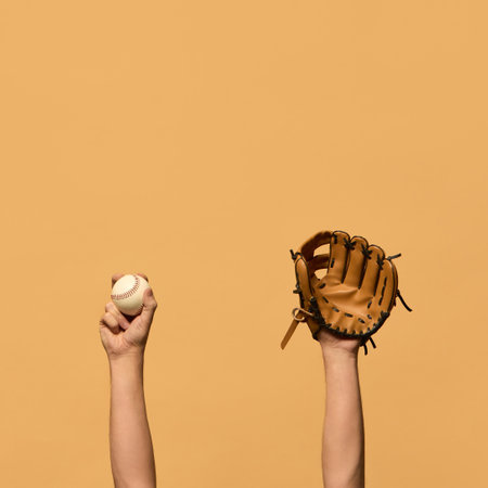 Raised hand in leather baseball glove, and gripping ball, symbolizing defensive preparation and teamwork against warm-toned background. Concept of sport equipment, control, strategy.の写真素材