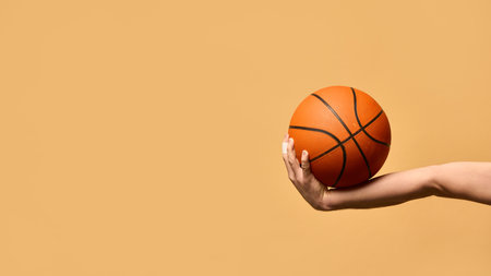Arm extended outward, gripping basketball firmly, demonstrating stability, technique, and readiness to make powerful play against warm-toned background. Concept of sport equipment, control, strategy.の写真素材