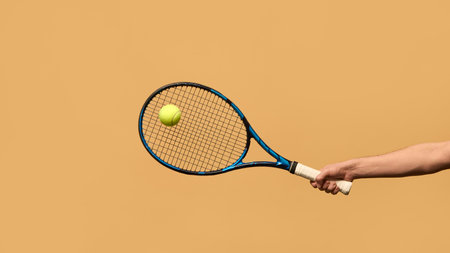 Outstretched arm holding tennis racket, ball hovering in front, representing concentration, timing, and perfect execution of stroke against warm-toned background. Concept of sport equipment, strategy.の写真素材