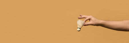 Hand delicately pinching white badminton shuttlecock, demonstrating finesse and accuracy in fast-paced badminton matches against beige background. Concept of sport equipment, control, strategy.の写真素材