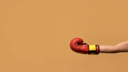 Arm extended with red boxing glove, fist clenched and slightly angled against warm brown background, emphasizing power and defensive strategy. Concept of sport equipment, control, strategy.の写真素材