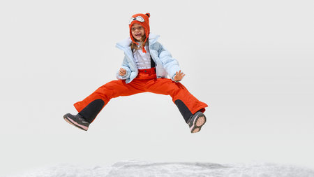 Happy, little kid, girl dressed colorful winterwear, jumping in motion of joy and happiness, with...