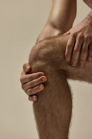 Close-up of strong male hands gripping knee in focused pose against warm studio background. Concept of natural beauty, fashion and style, health, masculinity.の写真素材