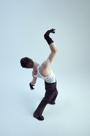 Aerial view of young man, dressed high-fashion outfit, moving elegantly raising hands against gradient background, highlight luxury style. Concept of self-expression and beauty. Adの写真素材