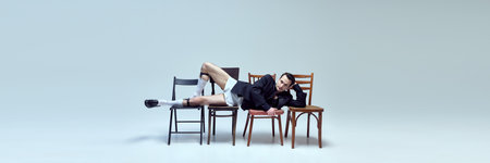 Banner. Artistic young man reclining across chairs with relaxed pose and playful confidence against...