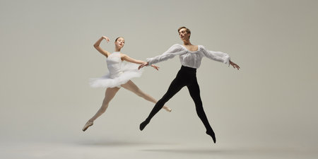 Dynamic photo of young ballet dancers in expressive leap, his flexible bodies angled in opposite...