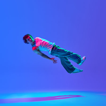 Talented breakdancer in action, defying gravity with dynamic mid-air moves against neon-lit blue...