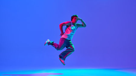 Talented and skilled young guy in casual clothes in motion, dancing breakdance against gradient blue...