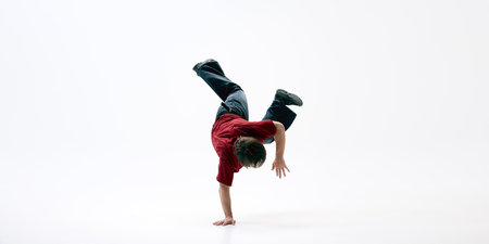 Dancer performing one-handed handstand, body in perfect control, and his legs bent in motion against white background. Concept of active lifestyle, street dance, passion, freestyle movement.の写真素材