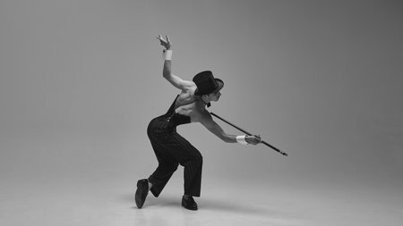 Monochrome. Expressive dancer in structured corset and tailored pinstripe trousers bending with animated elegance against white studio background. Concept of vintage style, movement, nostalgia.の写真素材