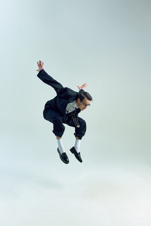 Young businessman jumping with bent legs and expressive pose against white studio background....