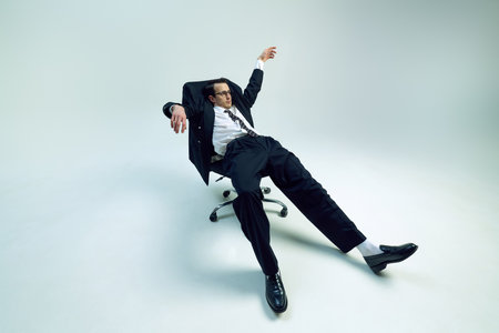 Young exhausted businessman reclining in rolling chair with loose posture and raised arm against white studio background. Concept of business, psychology, overworked, work-life balance.の写真素材