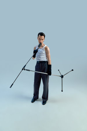 Young singer gripping microphone stand with intense focus, exuding timeless stage confidence against gradient studio setting. Vintage charisma. Concept of art, music, vintage, talentの写真素材