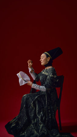 Elderly woman in historical noble dress carefully embroidering fabric with concentrated expression,...