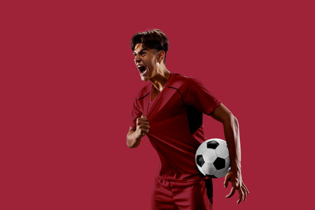 Energetic collage. Determined football athlete dressed in red expressing victory, gripping jersey, radiating power and energy against red background. Concept of sport, competition, passion, goal.の写真素材