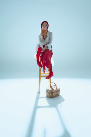 Young woman sitting on wooden stool, holding bread near face, gazing into distance, symbolizing...