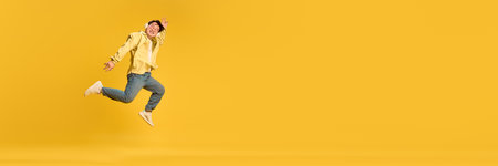 Banner. Energetic photo of young Asian man dressed casual attire. listening music and jumping of joy against yellow background with copy space. Concept of human emotions, sales, success. Adの写真素材