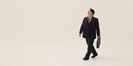 Dynamic photo of young attractive Asian man dressed formal attire walking with suit case, looking happy against white background. Concept of human emotions, business, entrepreneurship, law.の写真素材