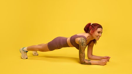 Focused woman holding forearm plank with perfect form against yellow studio background, working core...