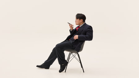 Serious and confident young Asian man, dressed smart-casual outfit sitting on chair and having...