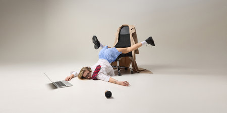 Office worker balancing upside down on chair, while working on laptop, reflecting instability of...