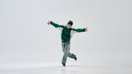 Cool attitude young guy, dancing hip-hop, spread arms wide, smoothly transitioning between moves against white background. Concept of music and dance, self-expression, sport art, urban culture.の写真素材