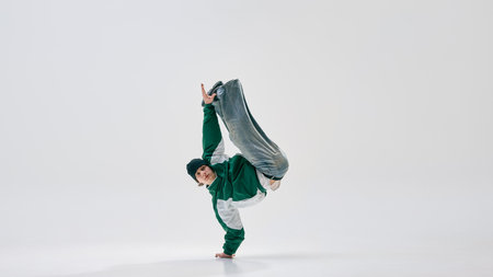 Performer, dressed retro attire, striking dynamic one-handed pose with legs airborne, showcasing strength against white studio background. Concept of sport, music, dance, discipline, creativity.の写真素材