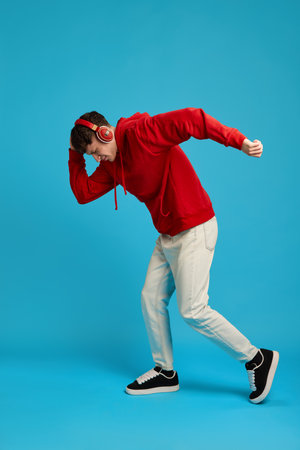 Full body photo of man dancing with red headphones on, expressing emotion and energy against blue background. Concept of music, movement, youth, style, social media trends, digital rhythm.の写真素材