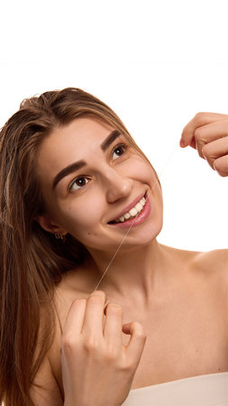 Portrait of young woman smiling, open mouth to clean teeth with white floss against white...