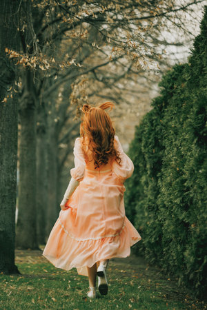 Running barefoot through alley of trees, fabric swirling like wind, young woman flees something unseen, yet eternal. Concept of escape, surreal time, freedom.の写真素材