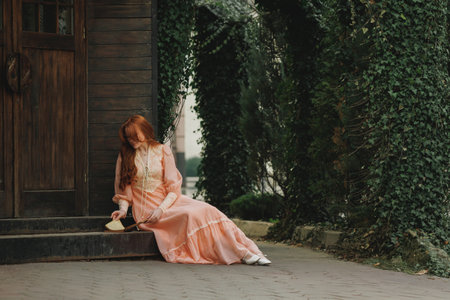 Sitting near wooden door, head bowed, she clasps an open book, vines curling around her like natures embrace. Concept of sorrow, reflection, mythic time. Suitable for book or movie cover.の写真素材