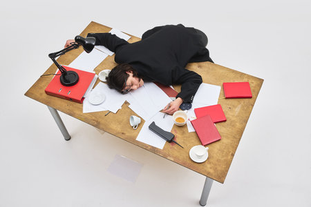 Aerial view of exhausted male employee collapsed on cluttered office desk with spilled coffee and...