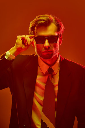 Close-up of young confident man lifting sunglasses with strong expression showing resistance and attitude. Concept of tension, masculinity, power, defiance, emotion, psychological wall.の写真素材