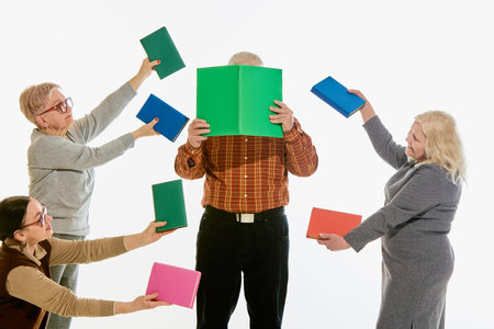 Man hidden behind giant book while three seniors offer more against white background, symbolizing overwhelming learning. Concept of modern pressure, senior study life, library.の写真素材