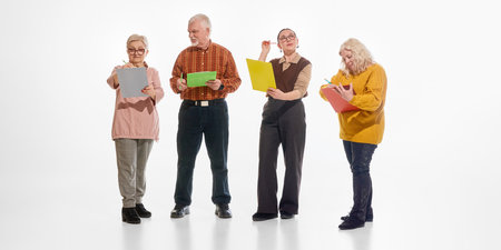 Group of senior students standing and writing, taking notes, on colorful clipboards against white studio background. Concept of education, adult learning, concentration, active minds in mature age.の写真素材