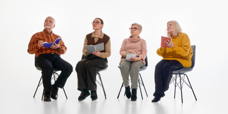Senior group, male and female pensioners, sitting on chairs with notebooks and listening attentively against white background. Concept of learning, concentration, pensioners in modern lifestyle.の写真素材