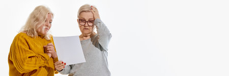 Banner. Two senior women looking at paper with worried expression against white studio background with negative space. Knowledge, news, financial issue or test results reaction, emotion concept.の写真素材