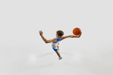 Basketball player jumping forward with explosive energy, one hand reaching back with ball, in...